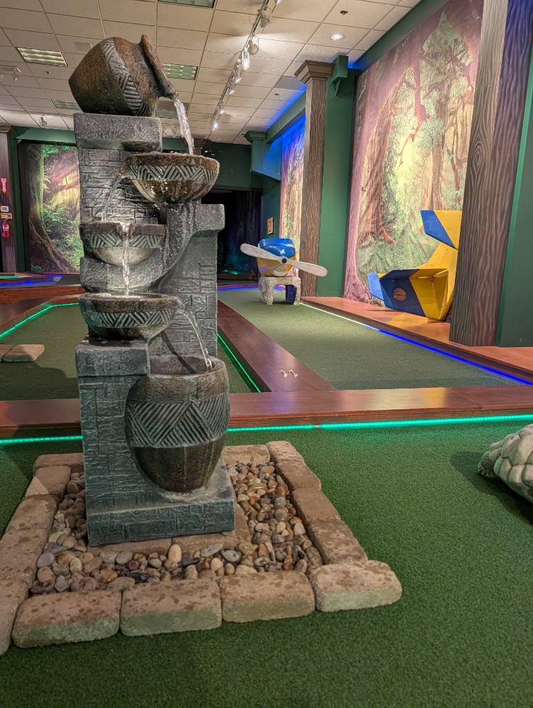 Indoor mini golf with water fountain and airplane propeller obstacle